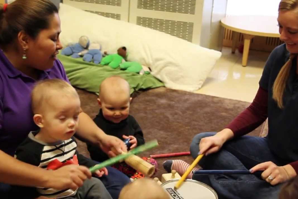 Daycare teachers teaching little babies music with drum and sticks.