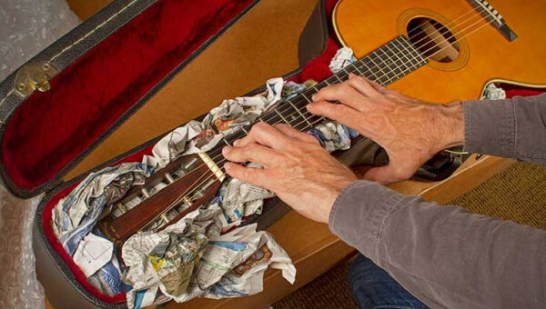A man (face not seen) packing his guitar in a box.