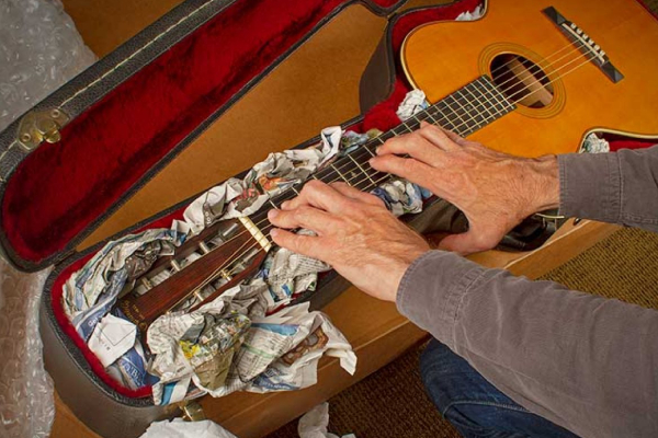 A man (face not seen) packing his guitar in a box.